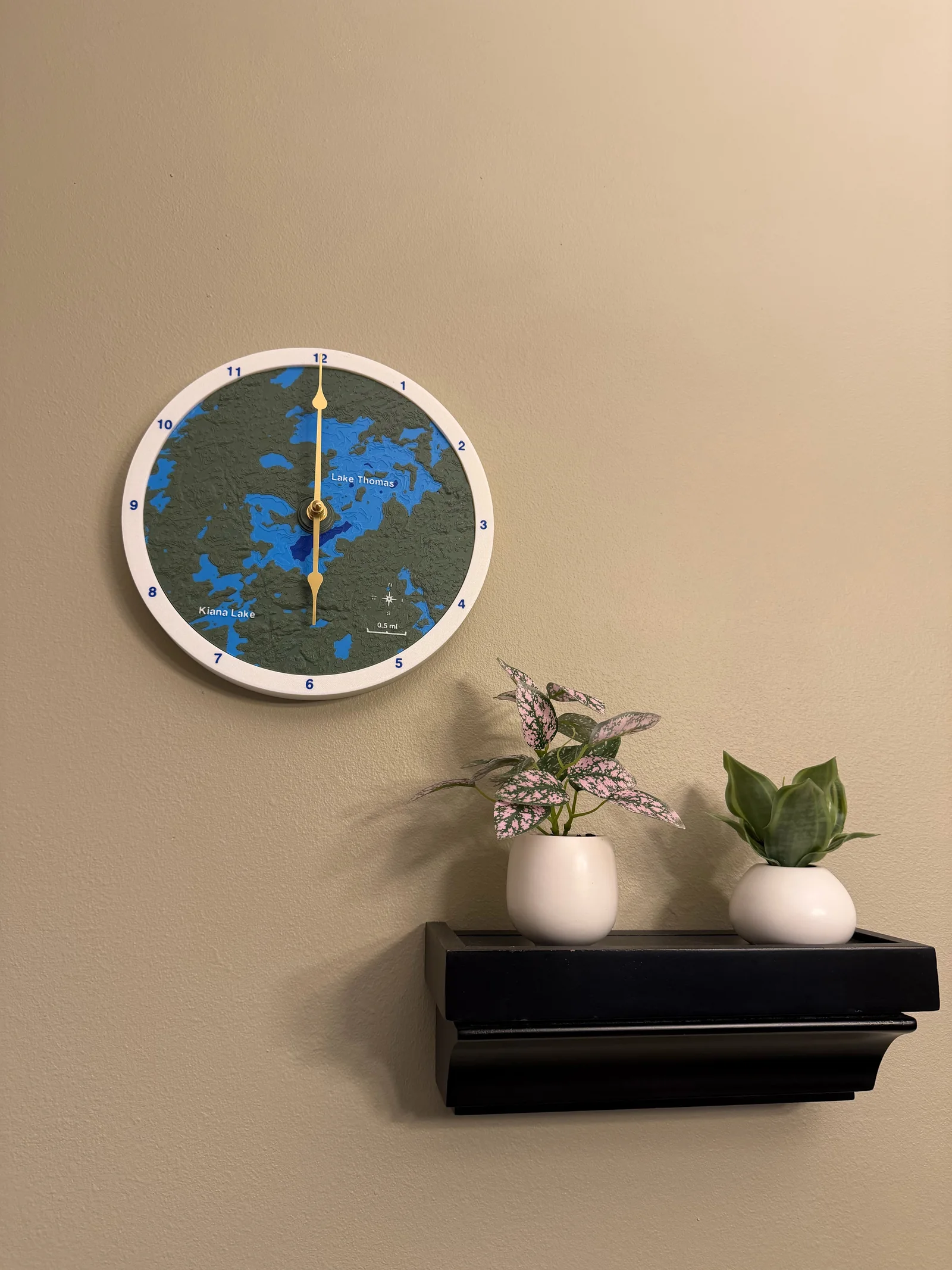 A finished topographic clock displayed at home, with a white rim around its lake landscape