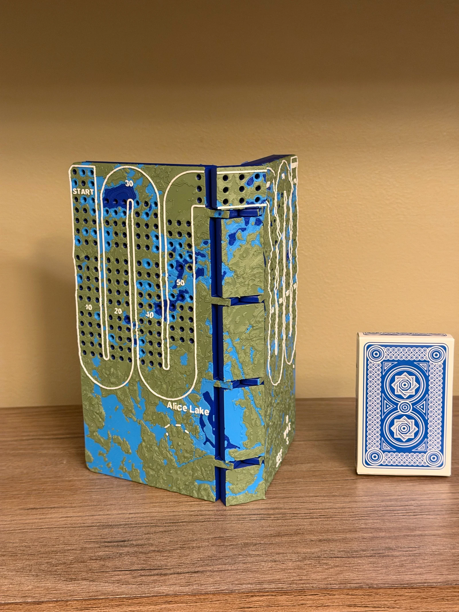 Full track folding Alice Lake cribbage board standing upright beside a deck of cards